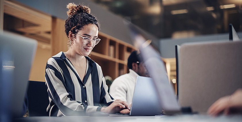 Jovem mulher estudando ou trabalhando em ambiente de escritório com computadores, foco na tecnologia a partir de uma ferramenta ITSM.
